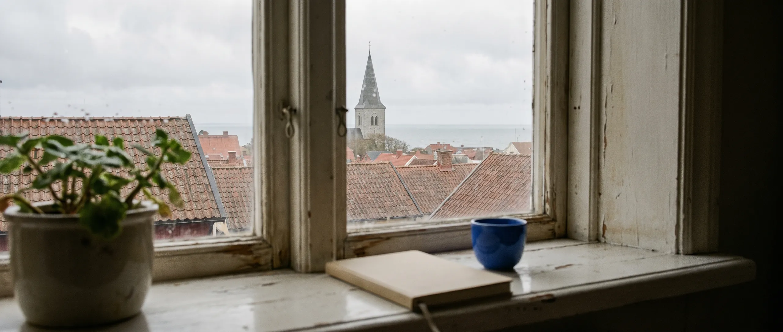 View from a window over rainy rooftops towards a church and the sea